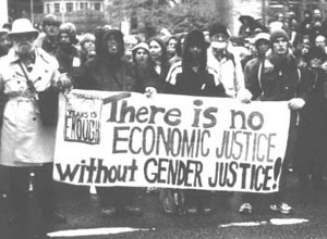 Black and white photo from march with a banner that reads "There is no economic justice without gender justice"